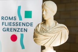 Eine weiße Büste einer römischen Frau, im Hintergrund das Logo der Landesausstellung