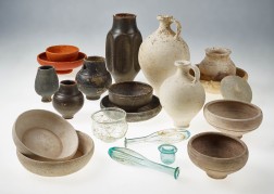 Mehrere Keramikgefäße in verschiedenen Größen und Farben sowie kleinere Glasgefäße stehen auf einem weißen Untergrund.