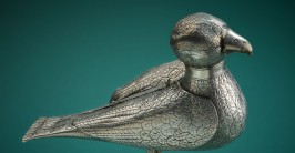 Eine silberne Figur eines Vogels vor einem dunkelgrünen Hintergrund