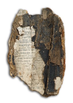 Ein brüchiges Papierfragment mit Schriftzeichen in Fraktur und Hebräisch darauf.