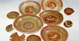 Mehrere runde Keramikschalen- und Teller von rötlicher Farbe mit grünlich-gelben Verzierungen
