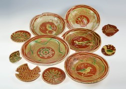 Mehrere runde Keramikschalen- und Teller von rötlicher Farbe mit grünlich-gelben Verzierungen