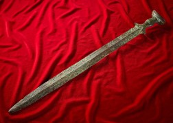 Ein grünliches Schwert, das auf einer roten Samtdecke liegt.