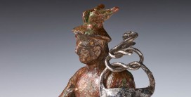 Eine bräunliche kleine Statuette, die den römischen Gott Merkur zeigt mit geflügeltem Hut und Stab in der Hand.