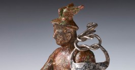 Eine bräunliche kleine Statuette, die den römischen Gott Merkur zeigt mit geflügeltem Hut und Stab in der Hand.
