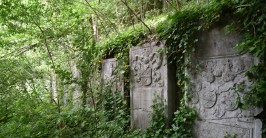 Mehrere zugewachsene Grabsteine vor einer Wand aus grobem Mauerwerk