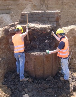 Arbeiter schaufeln Erde aus einem runden Mauerwerk
