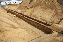 ausgegrabene römische Wasserleitung in Baugrube mit arbeitenden Archäologen
