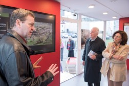 Ein Mann steht vor einem Monitor in dem Container und erkl&auml;rt zwei anderen Personen etwas.