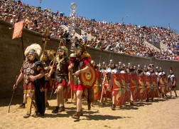 Eine Gruppe Römersoldaten marschiert in einer Arena vor vollbesetzter Tribüne